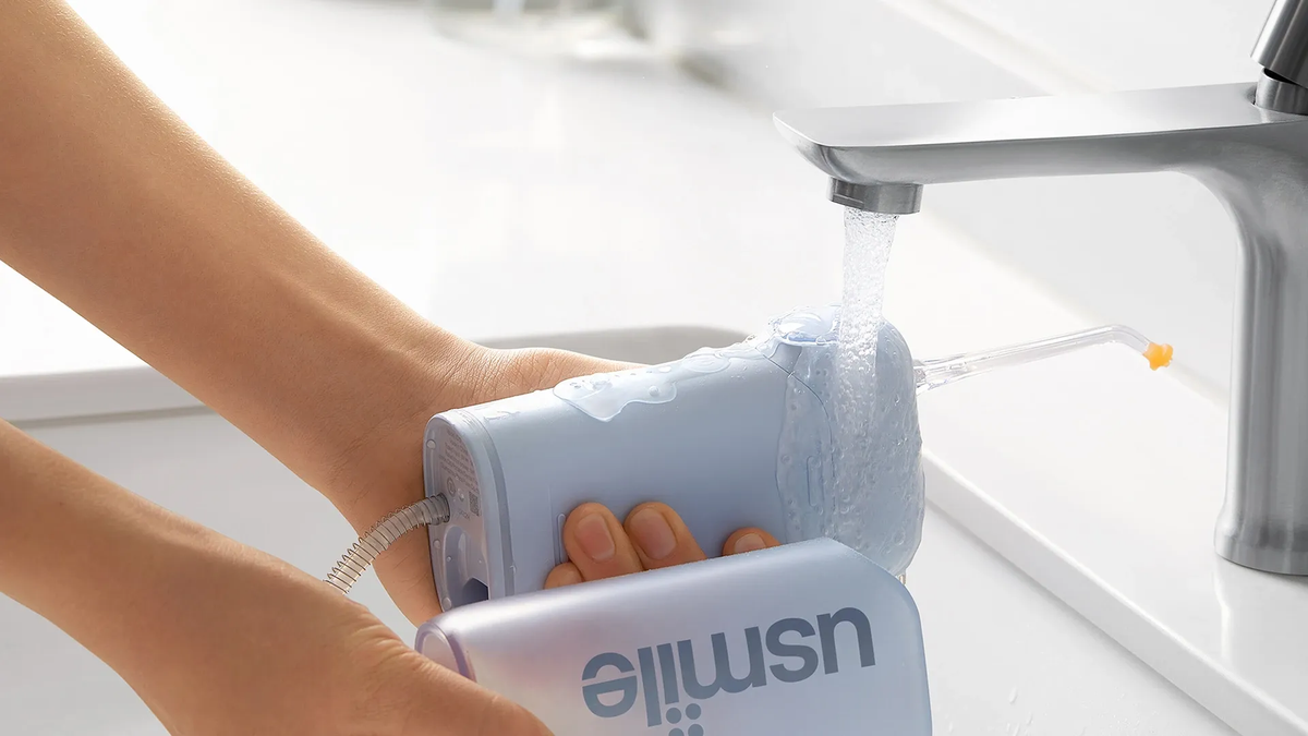 Person rinsing a light blue usmile water flosser under a running faucet