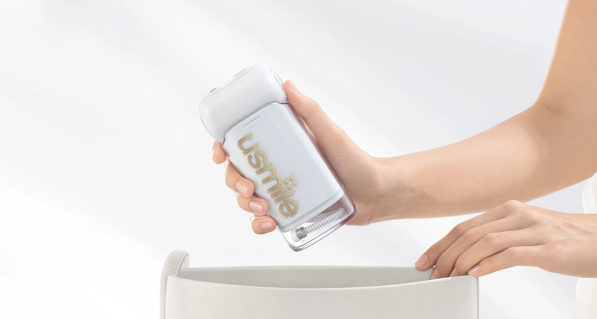 Person holding a usmile portable water flosser over an open waste bin