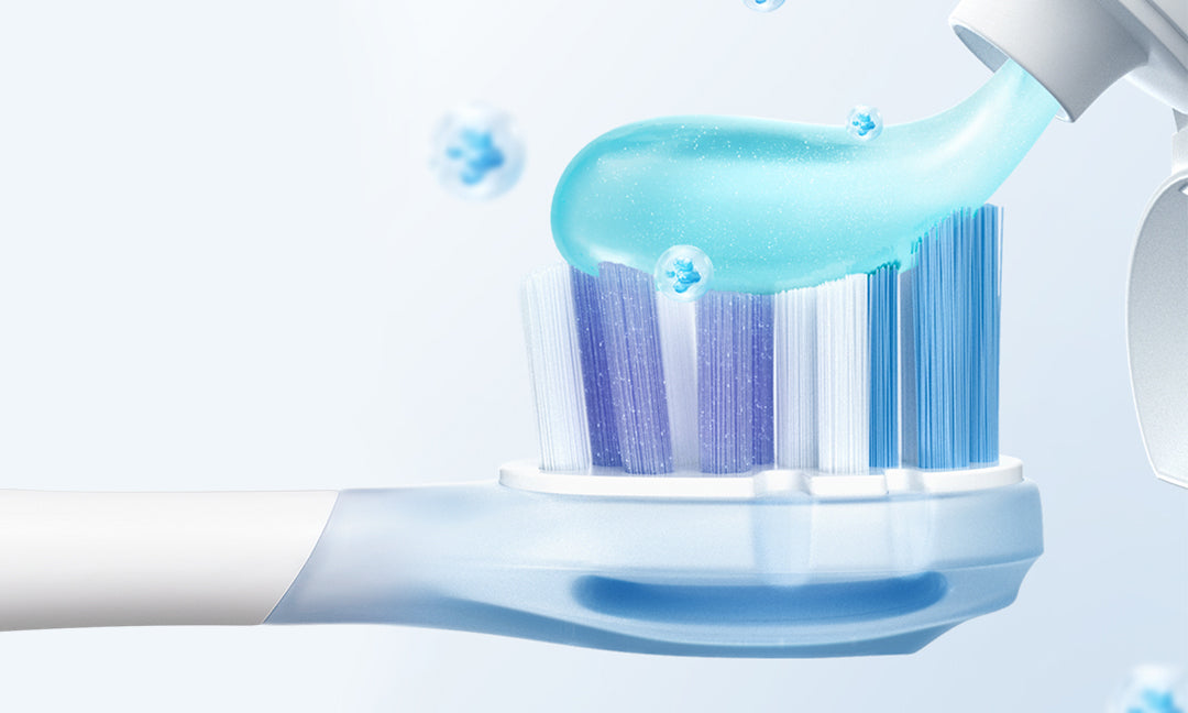Toothpaste being applied to the blue and white bristles of an electric toothbrush head
