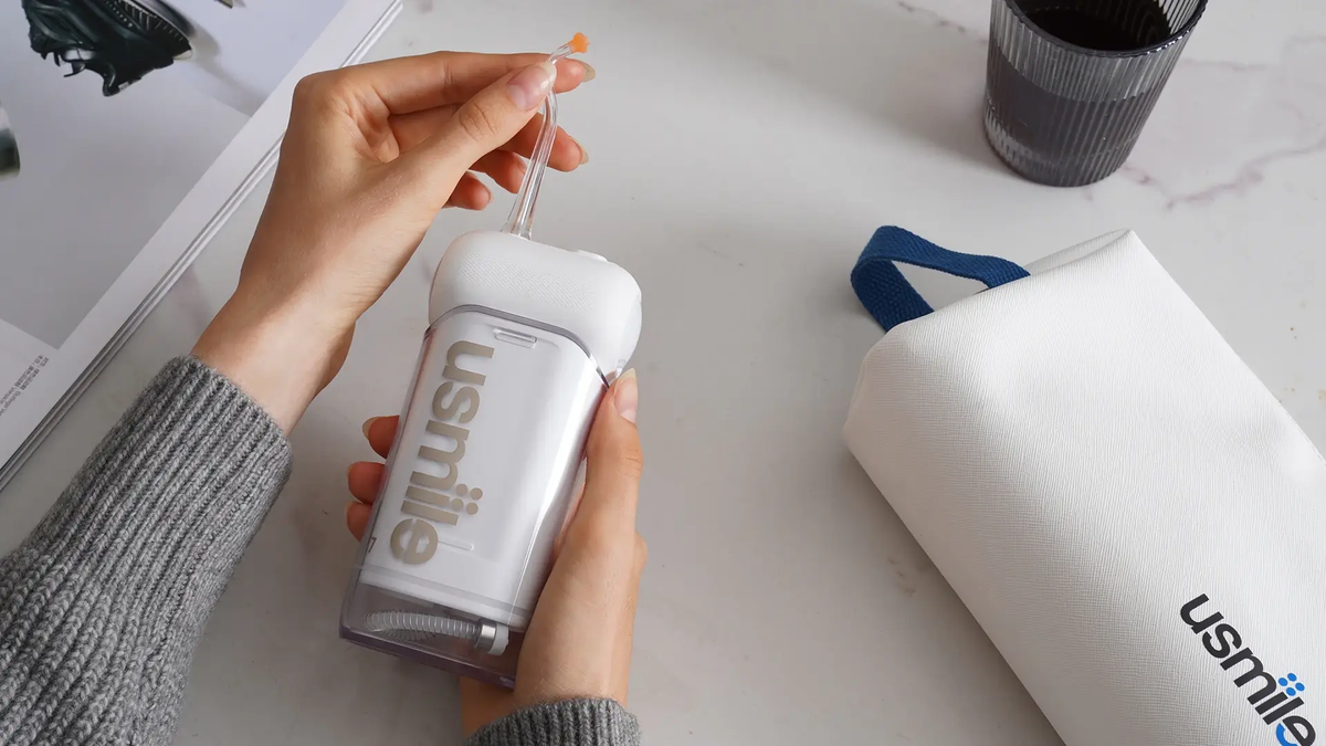 Hands fitting a nozzle onto a white usmile water flosser beside its travel bag