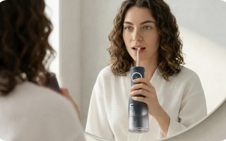 Woman using a black usmile water flosser while looking in a bathroom mirror